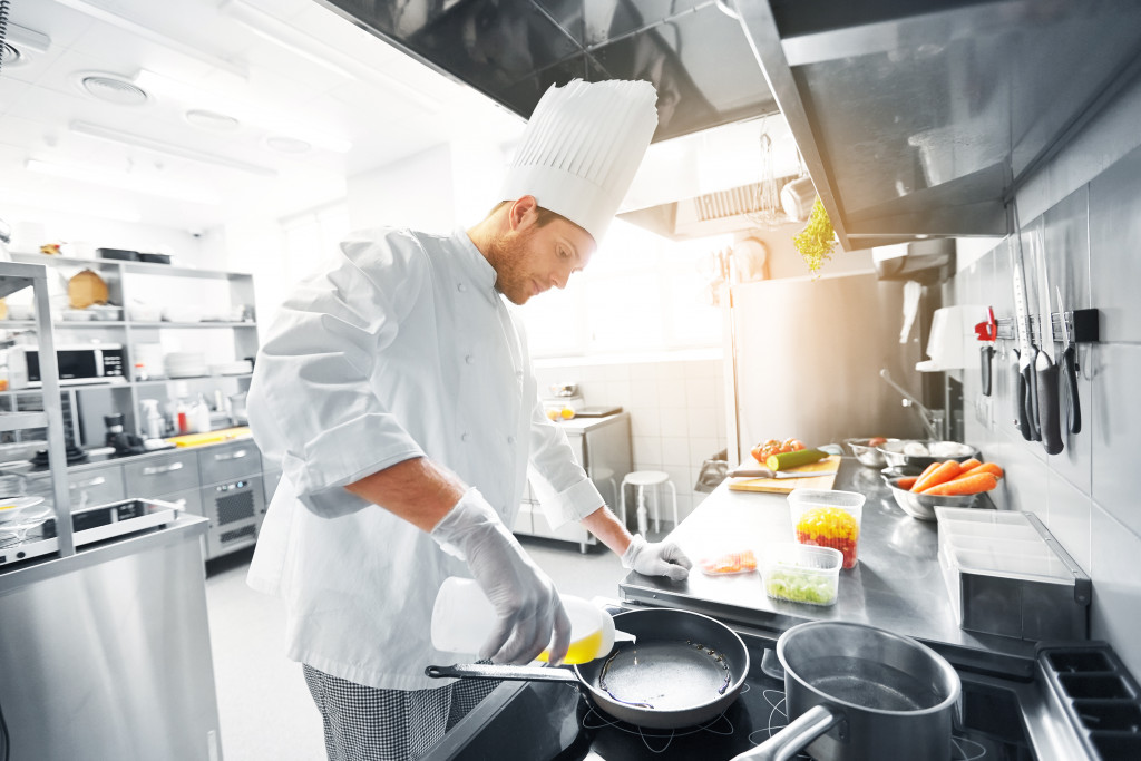 a male chef in the ktichen placing a cooking oil in a pan