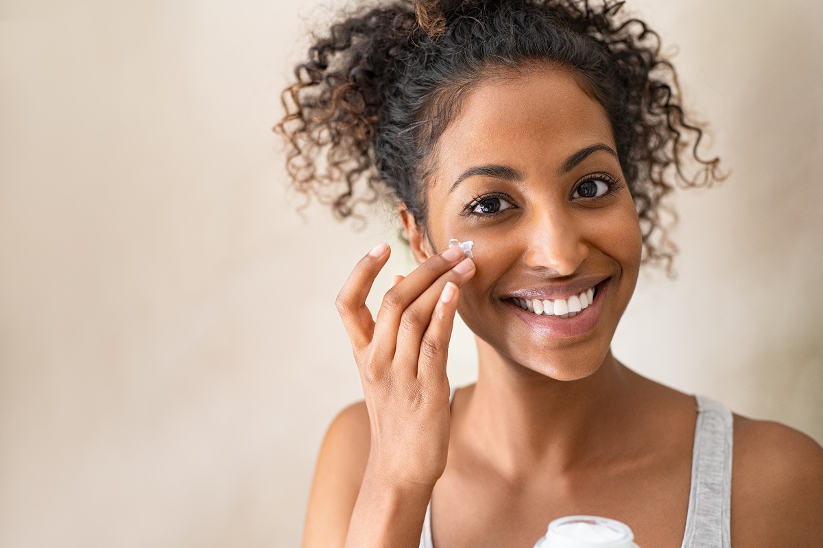curly haired woman adding cream to her face across a mirror