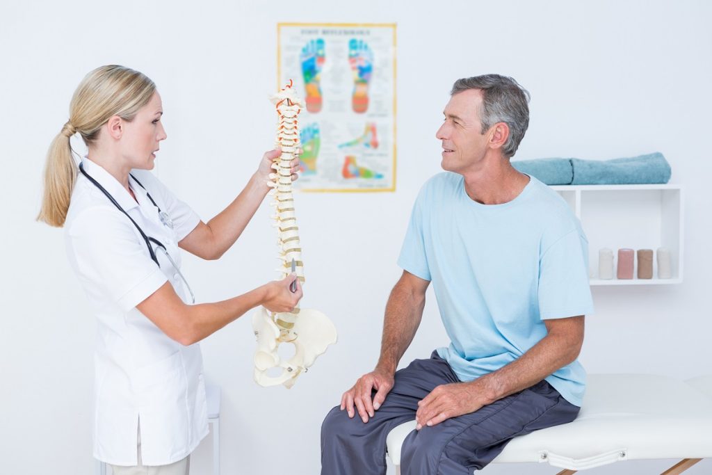 female doctor holding a spine model in front of a senior patient